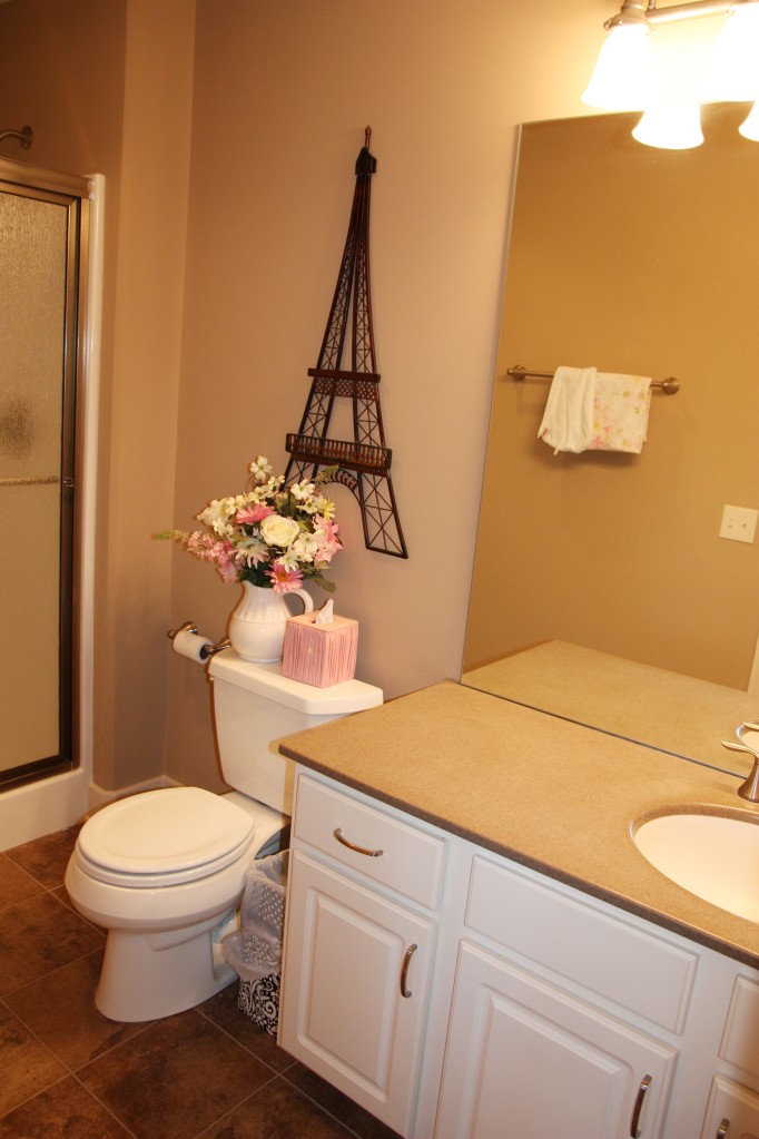 A white and cream colored bathroom with an Eiffel Tower on the wall.