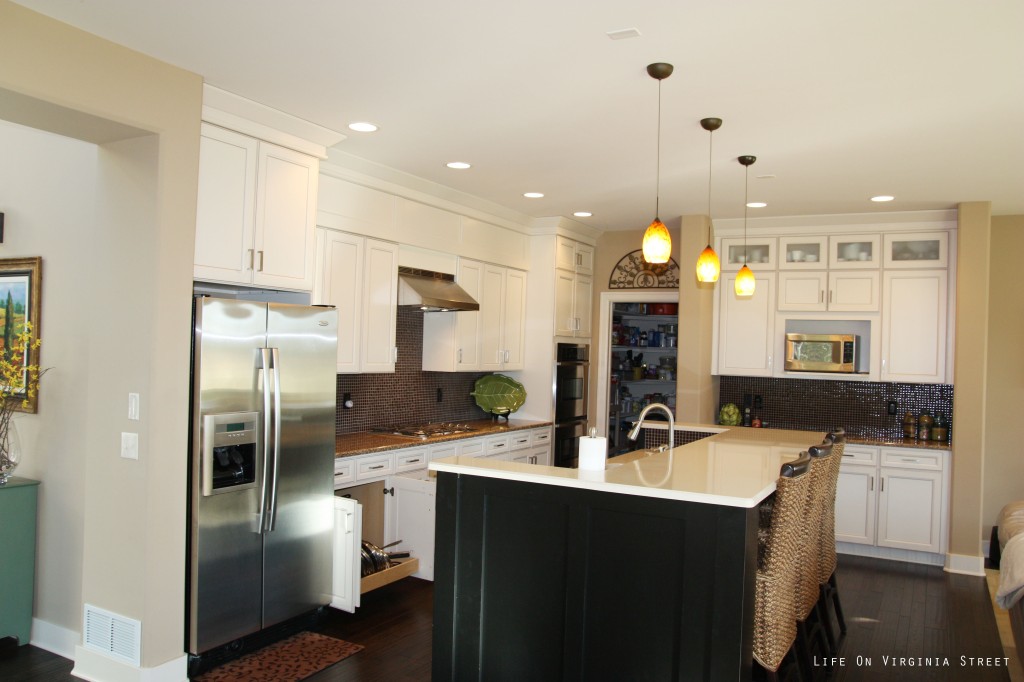 Large kitchen island with dark wood and light counter tip, a stainless steel fridge and white cabinets.